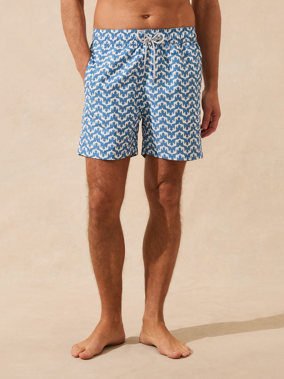 Front view of man wearing blue swim shorts with elephant pattern on a beige background
