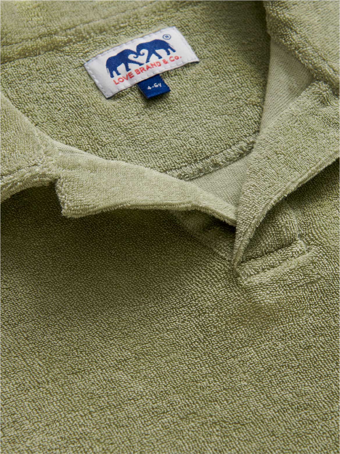 Close-up of a kids green terry polo shirt showing a brand label featuring two elephants and collar.