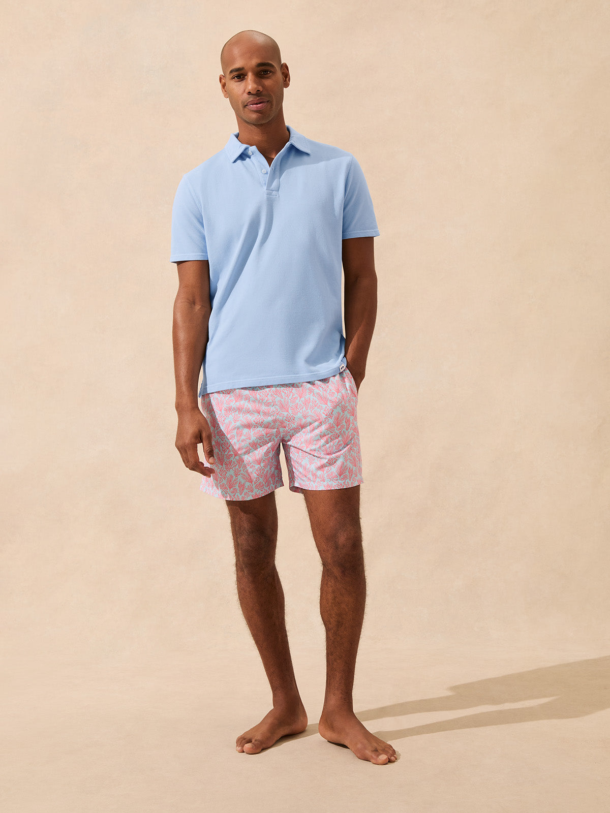 Man wearing a light blue polo shirt and pink coral swim shorts