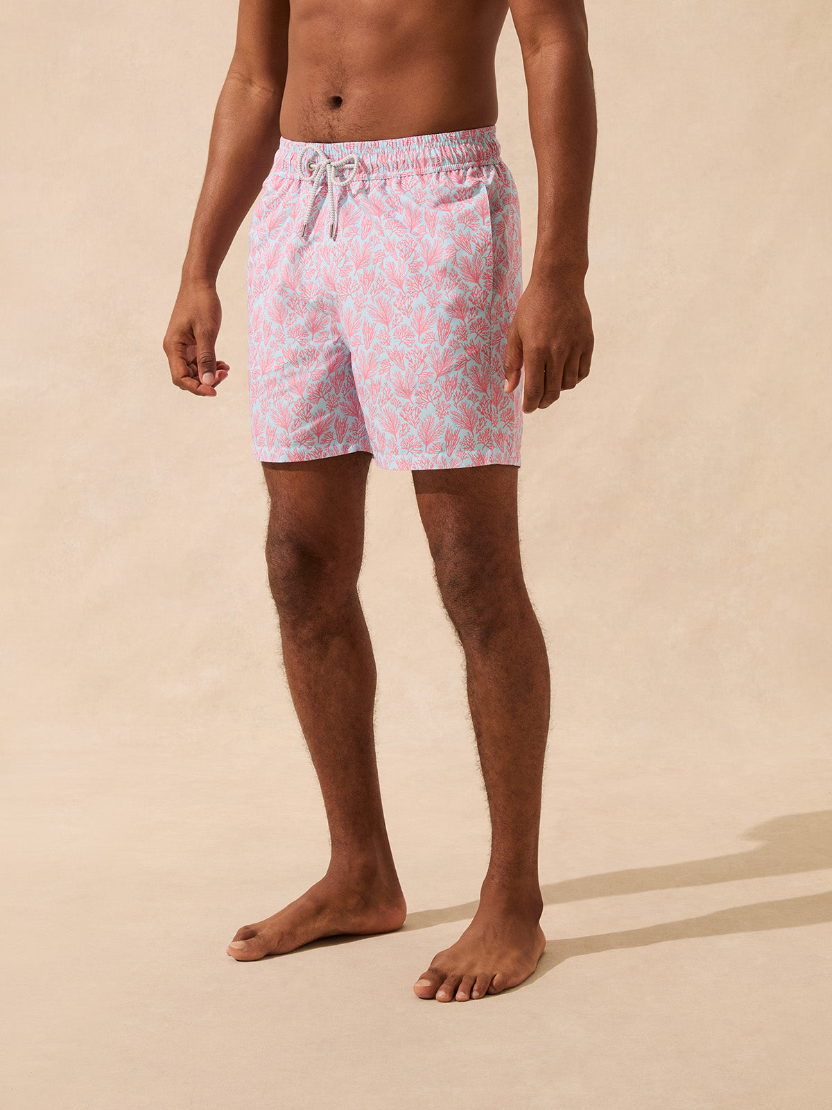 Front view of man wearing light blue swim shorts with a pink coral pattern