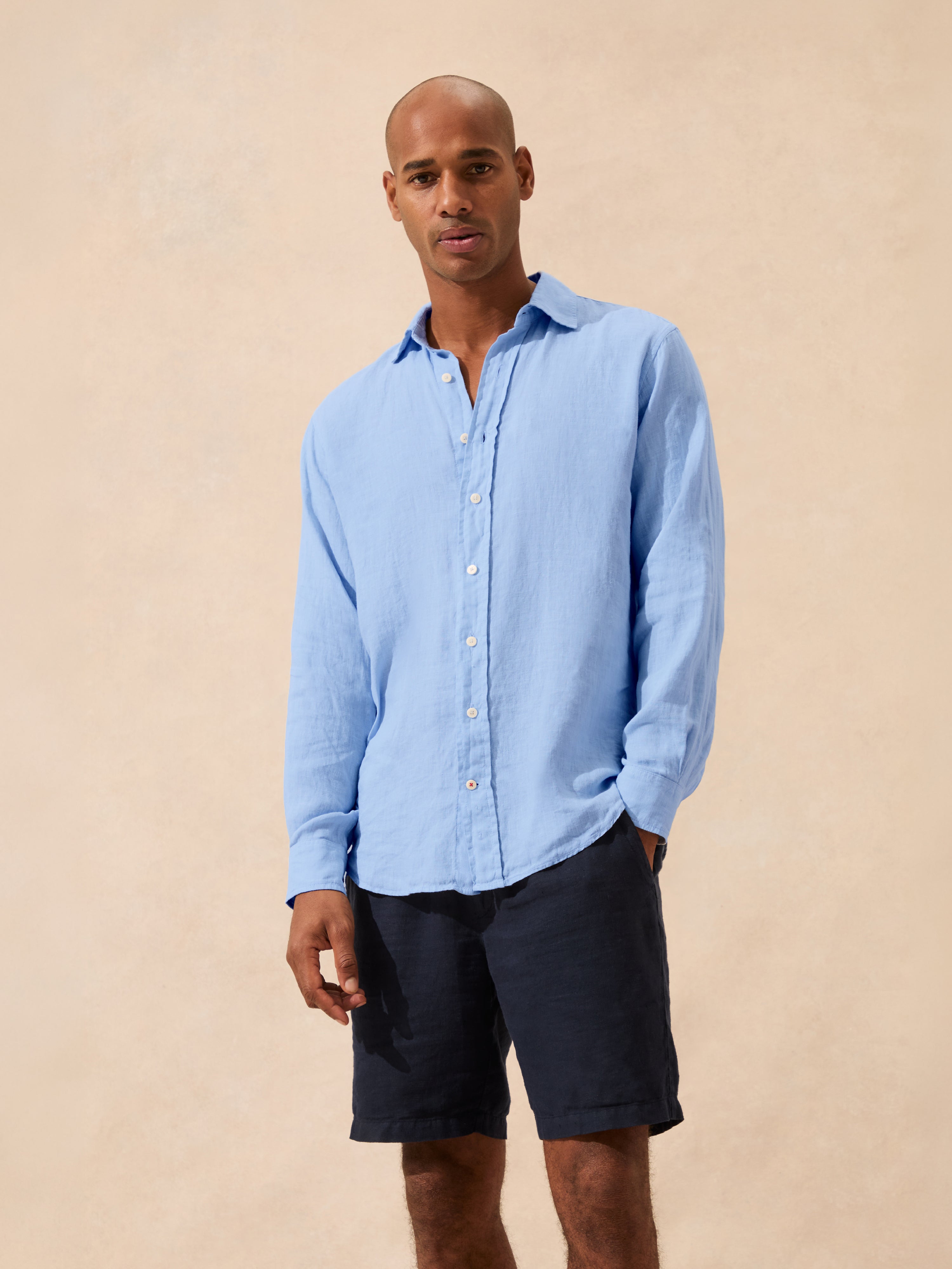 Man wearing a light blue shirt and dark shorts against a beige background