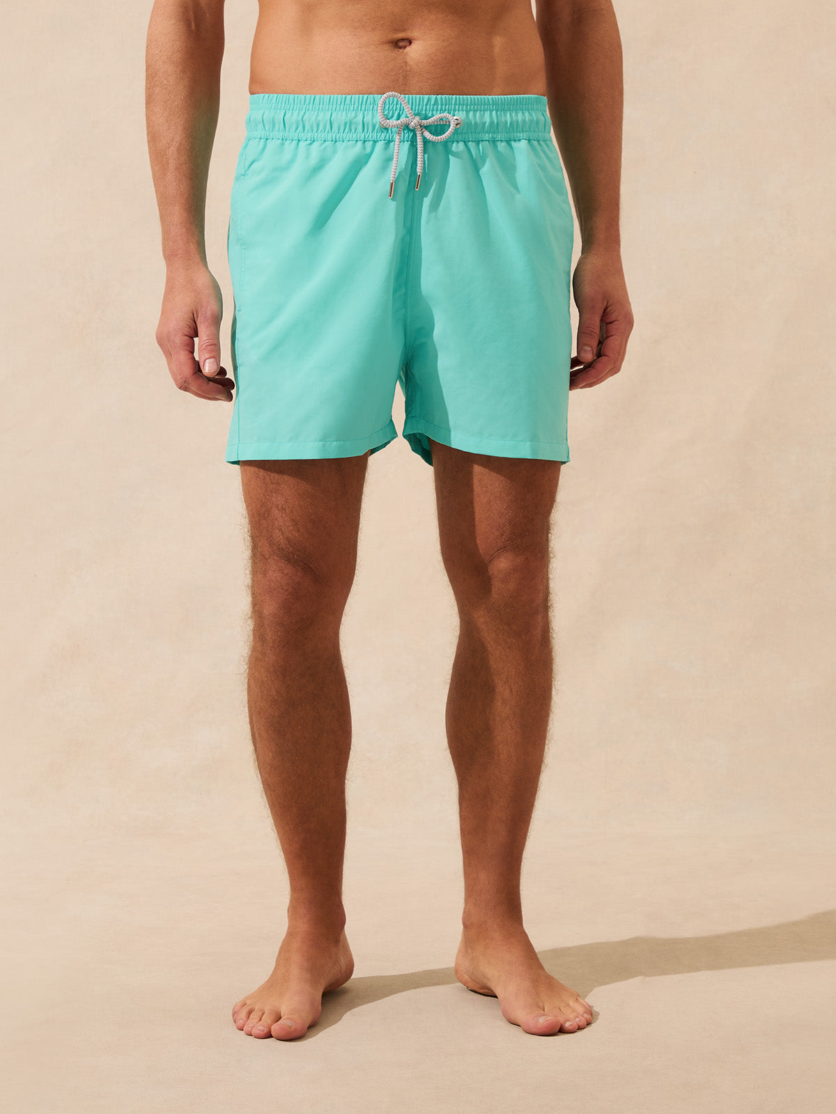 Man wears mint green swim shorts against a beige background