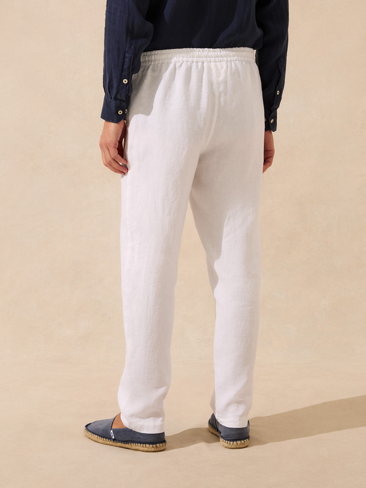 Man wearing white linen trousers and a navy shirt on a beige background