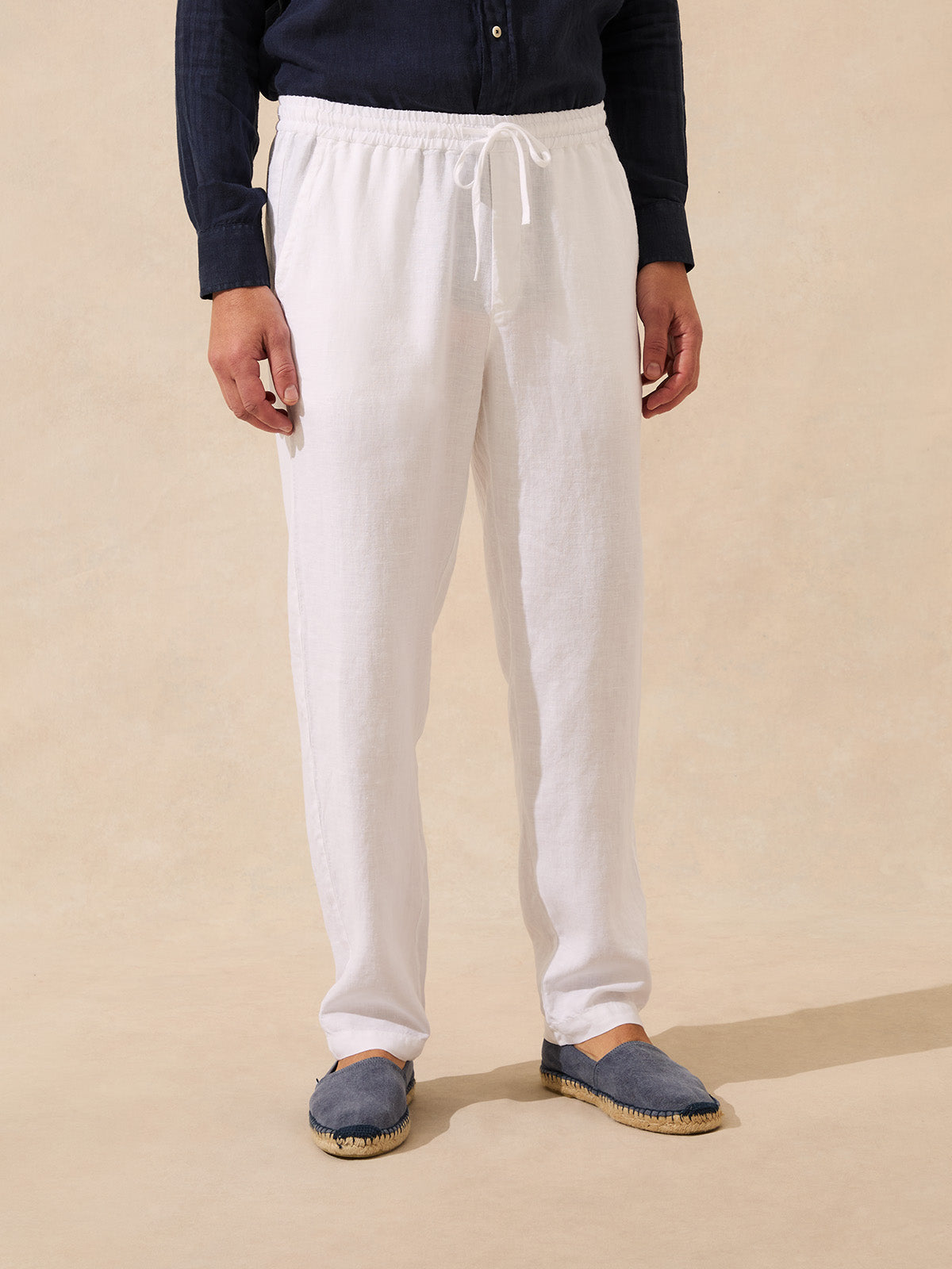 Man wearing white linen trousers and espadrilles on a beige background