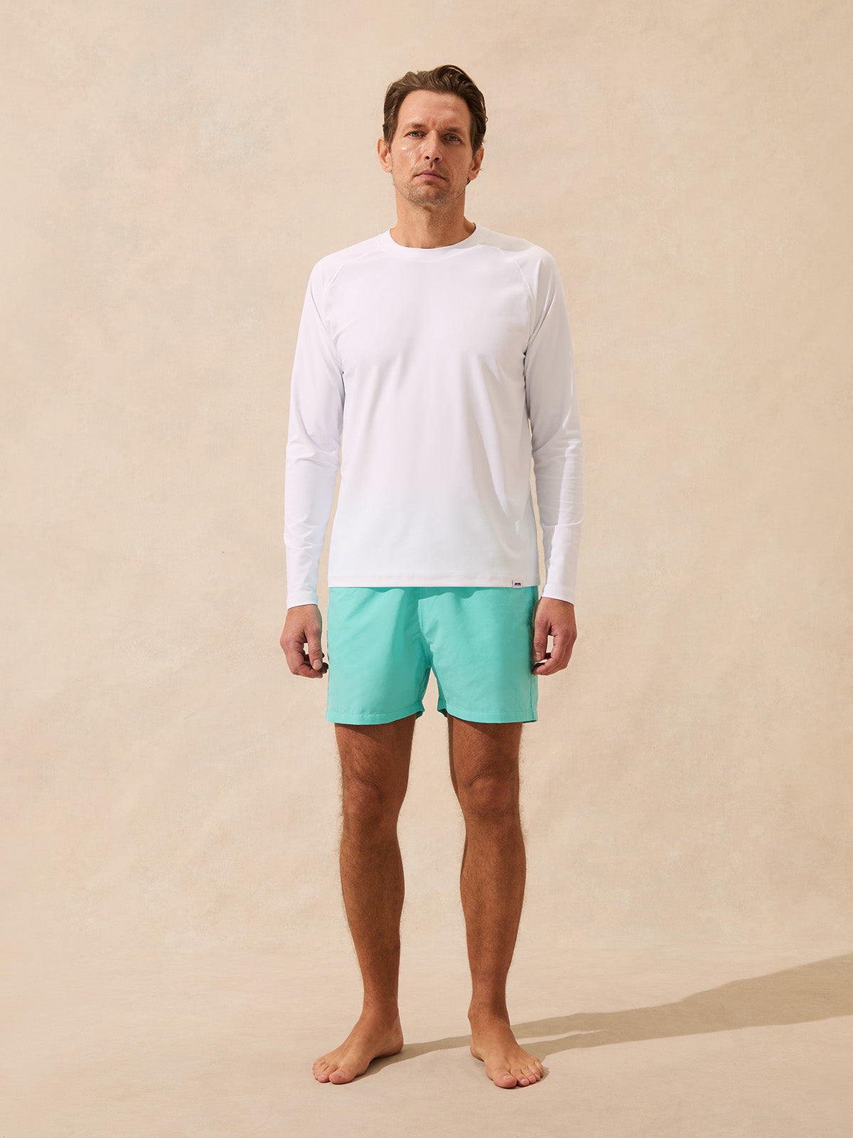 Man wears a white rash vest with long sleeves paired with mint green swim shorts