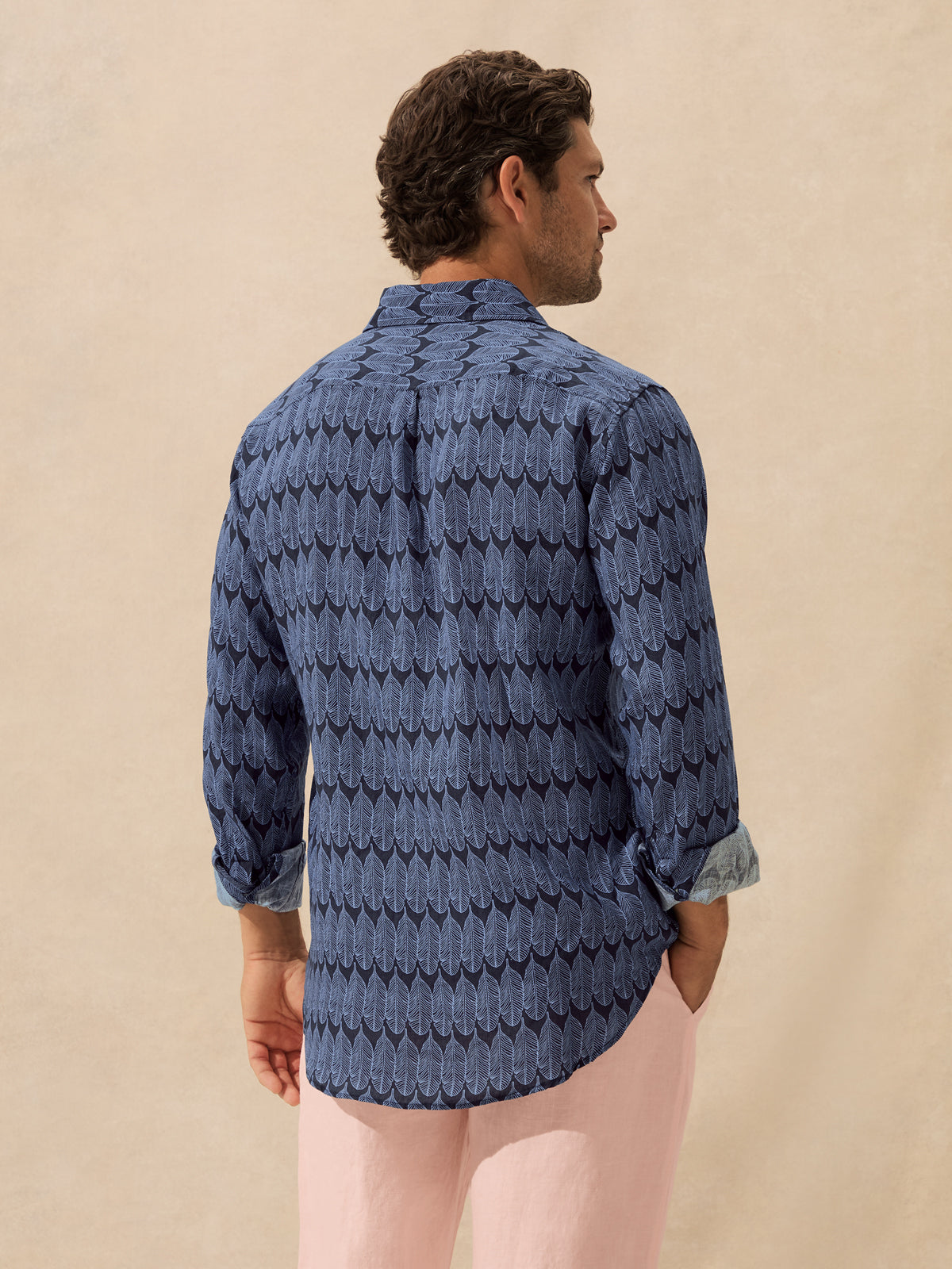 A man shown from the back wearing a blue patterned long-sleeve shirt.