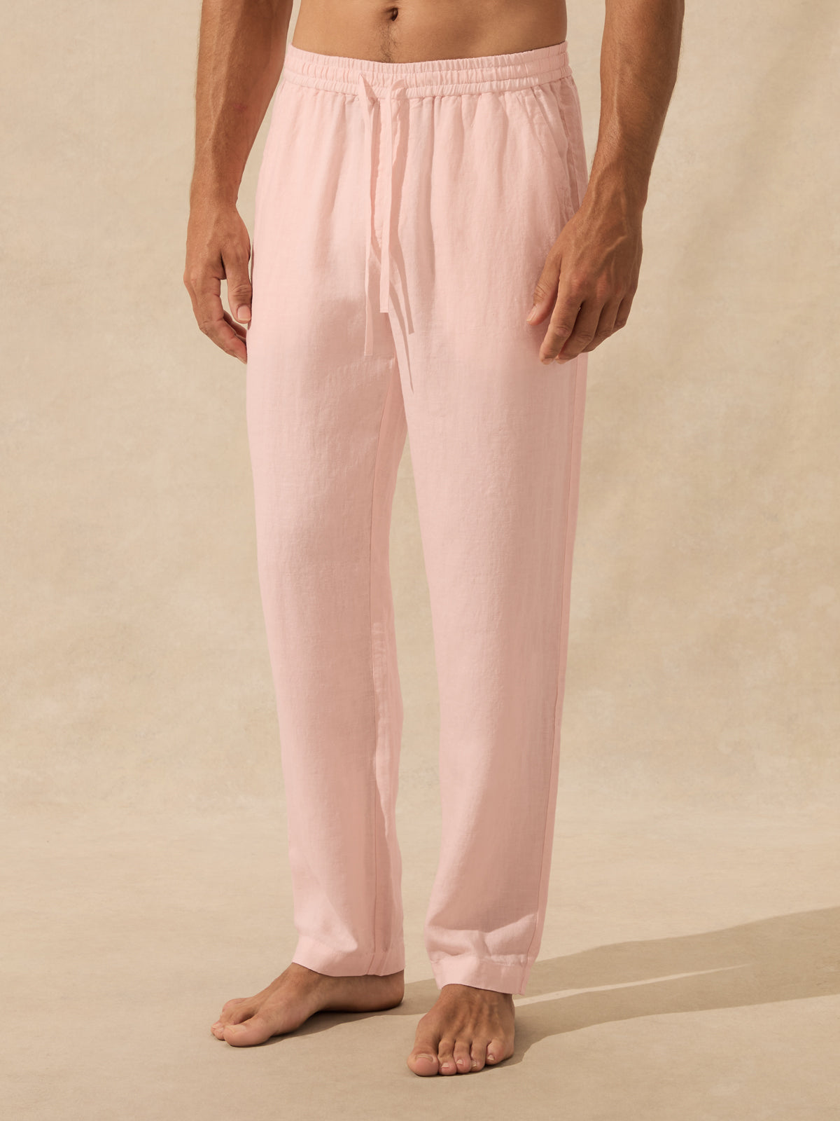 A person wearing light pink drawstring lounge pants, shown from the waist down against a warm beige studio background.