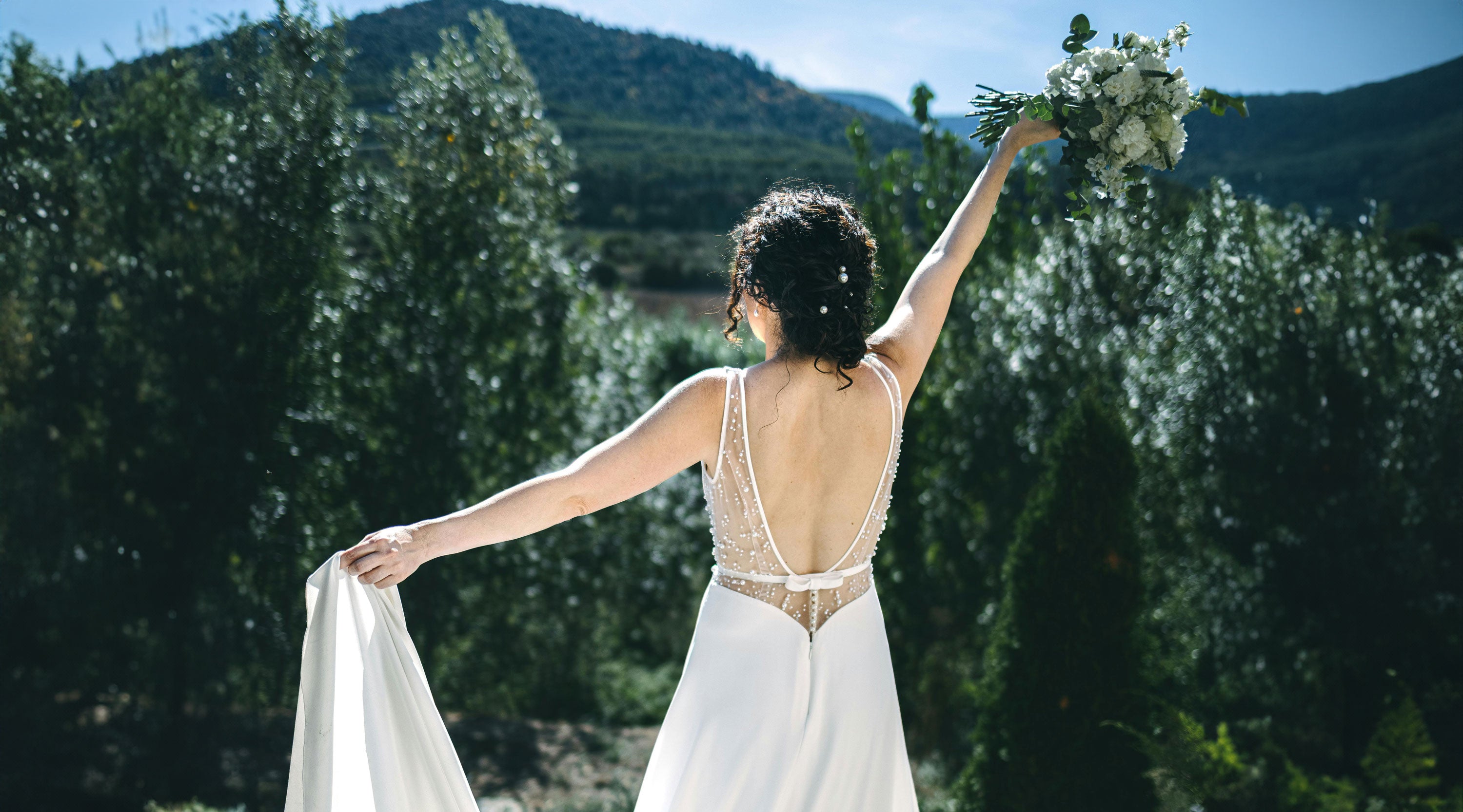 Woman in a white wedding dress holding a bouquet with a scenic background