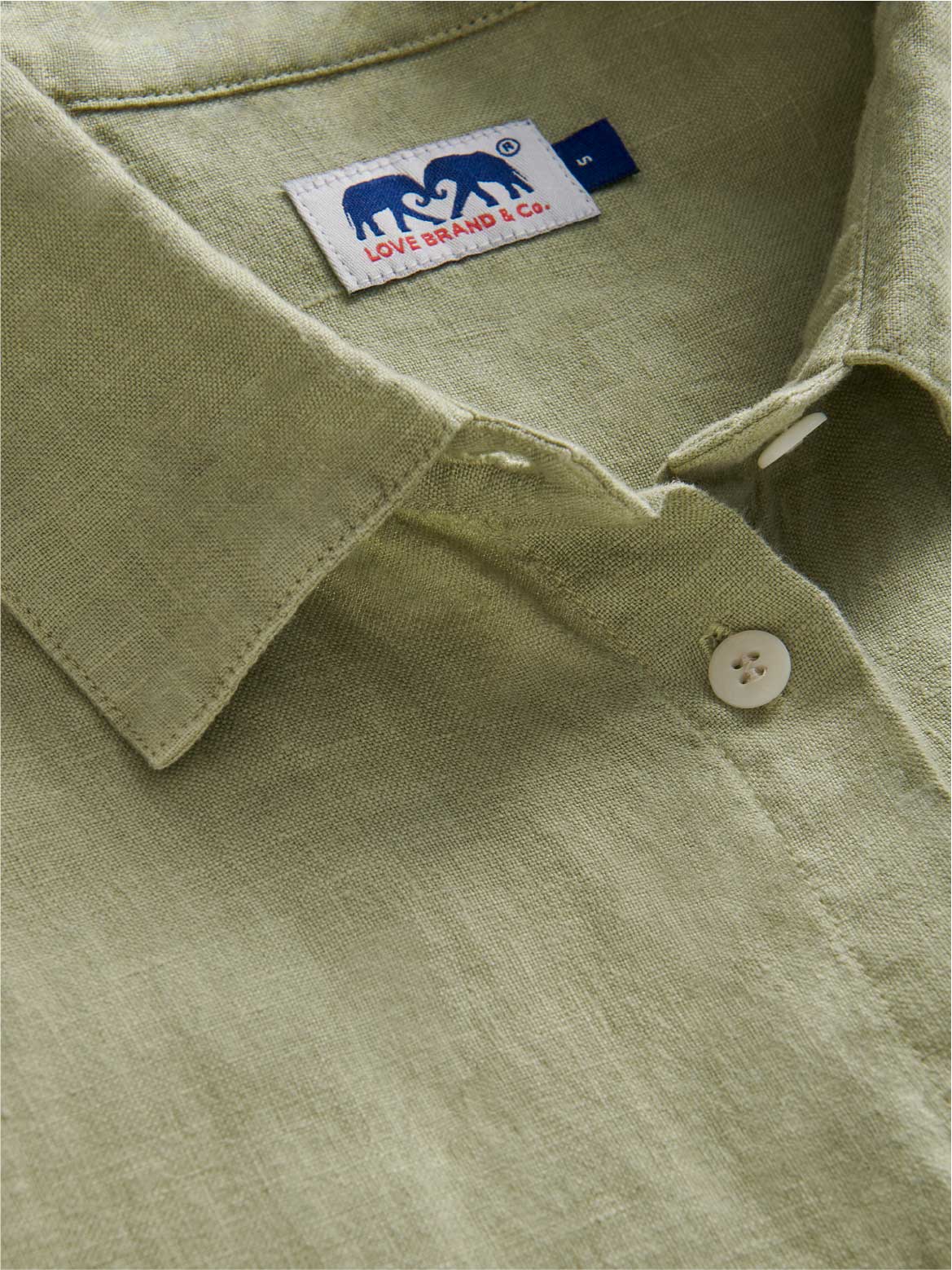 Close-up of a green linen shirt dress with a brand label on the collar.