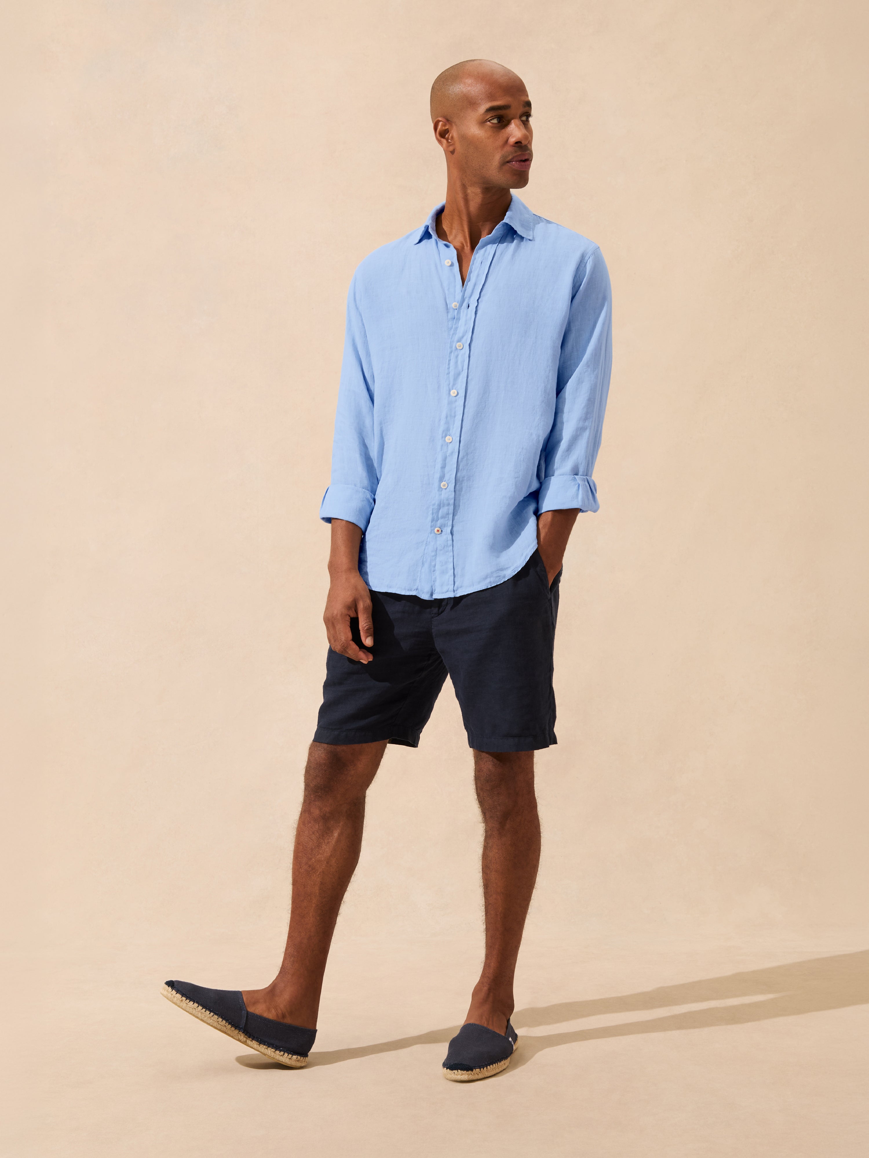 Man wearing a light blue shirt and navy shorts on a beige background