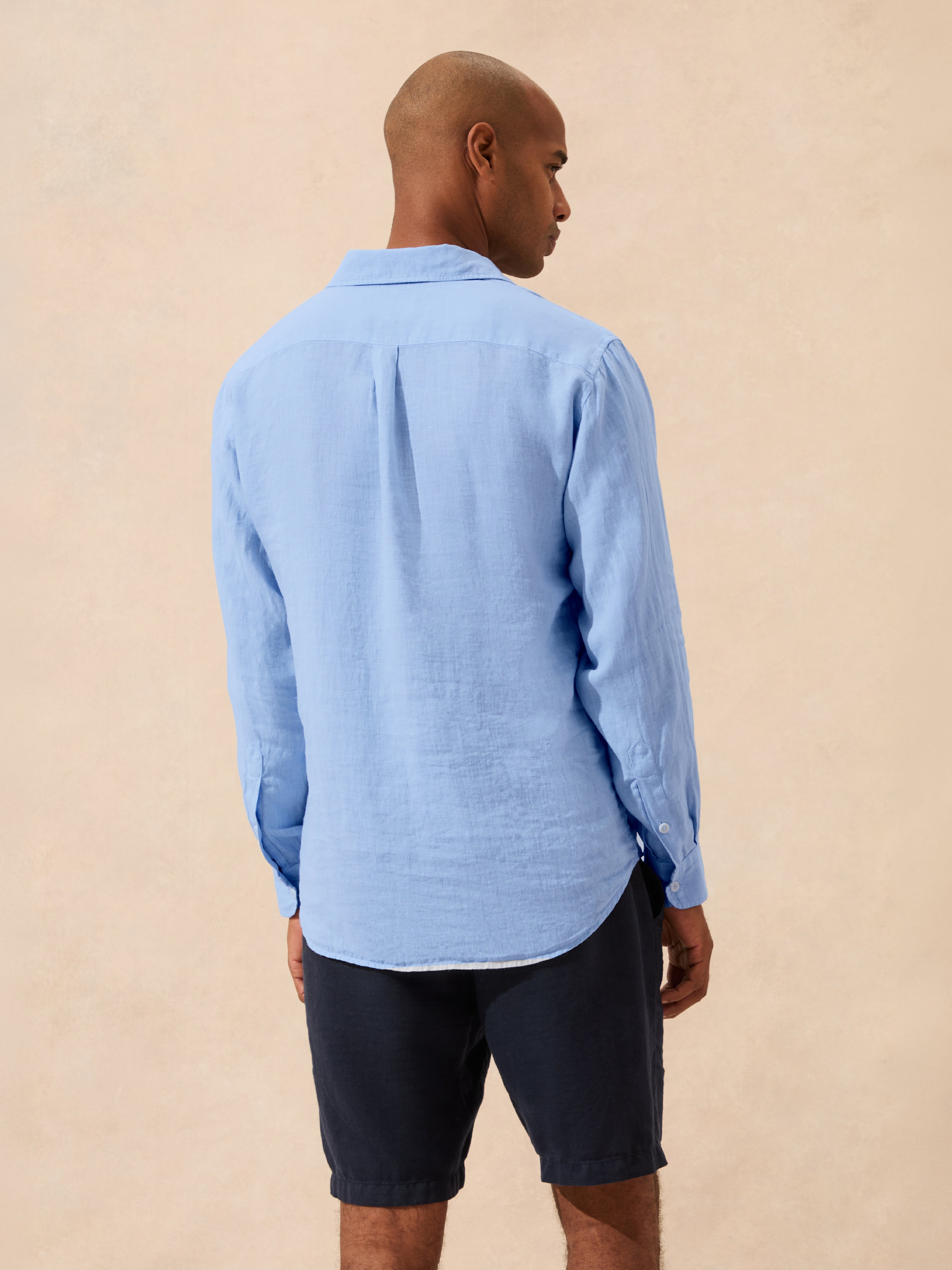 Man wearing a light blue shirt and dark shorts on a beige background
