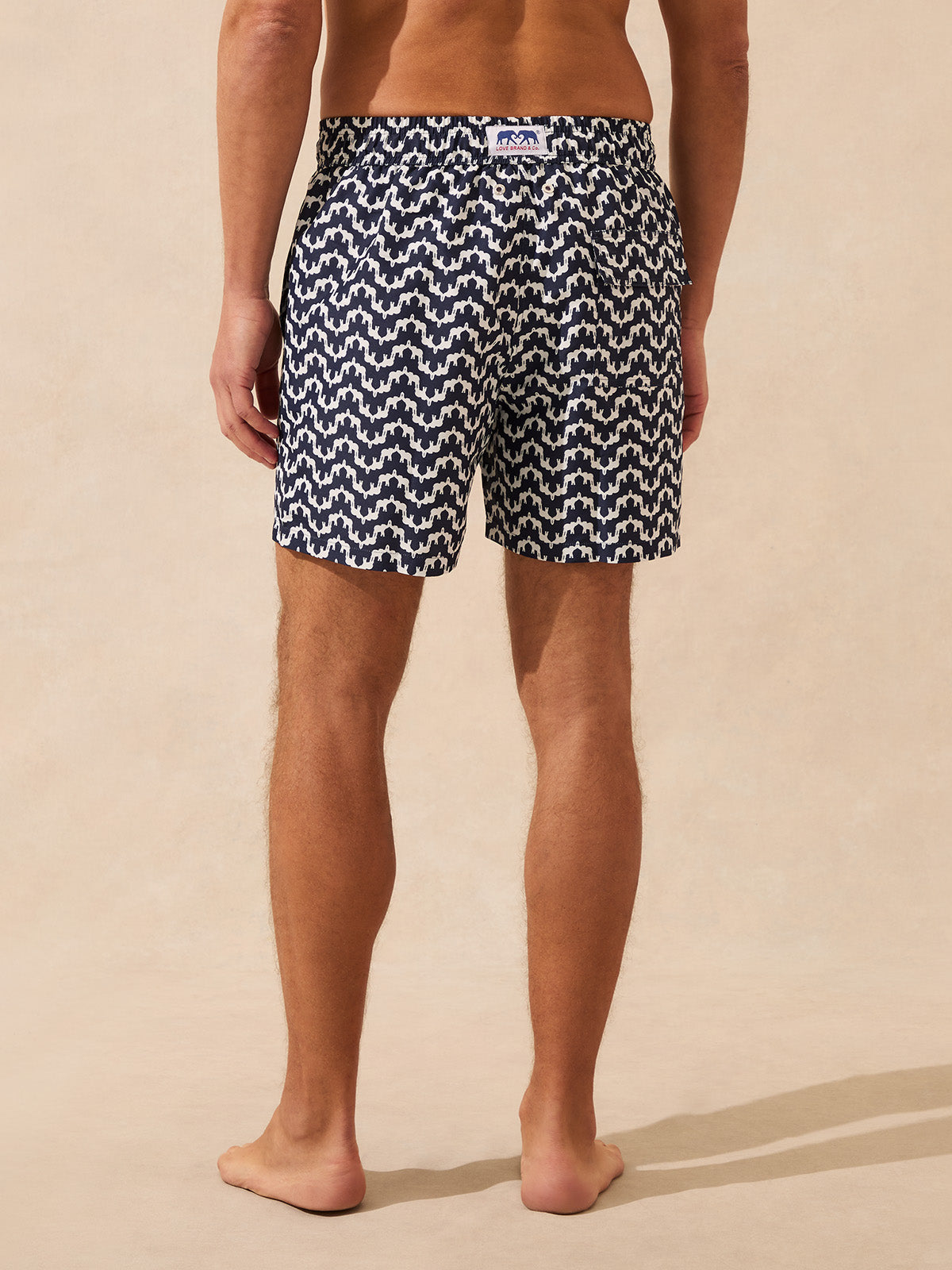Man wearing black and white patterned swim shorts on a beige background