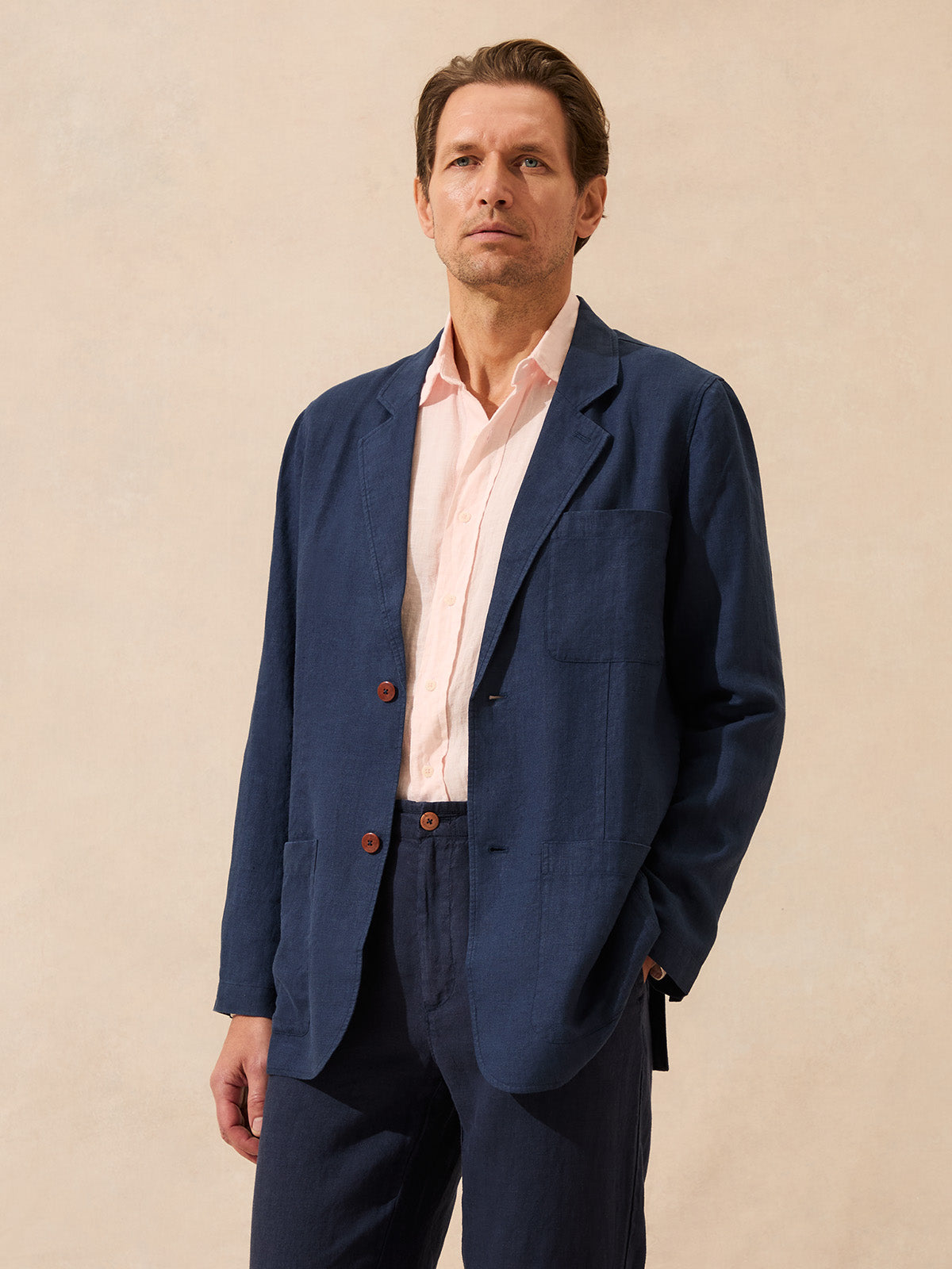 Man wearing a blue blazer over a pink shirt on a beige background
