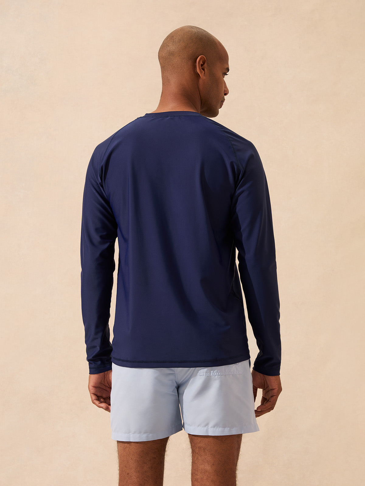 Man wearing a navy rash vest with long sleeves against a beige background