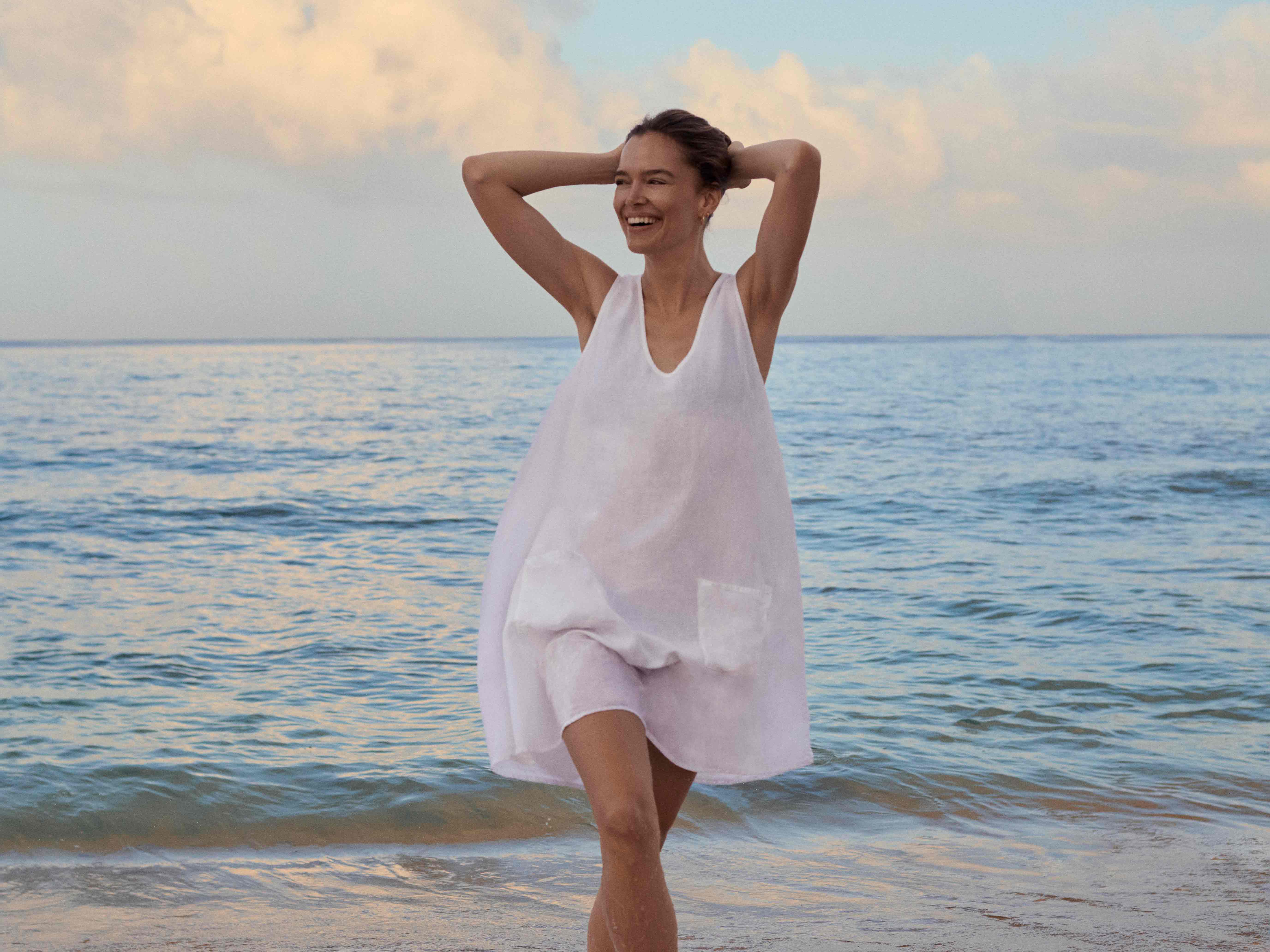 Woman in a white dress standing on a beach with ocean and sky in the background