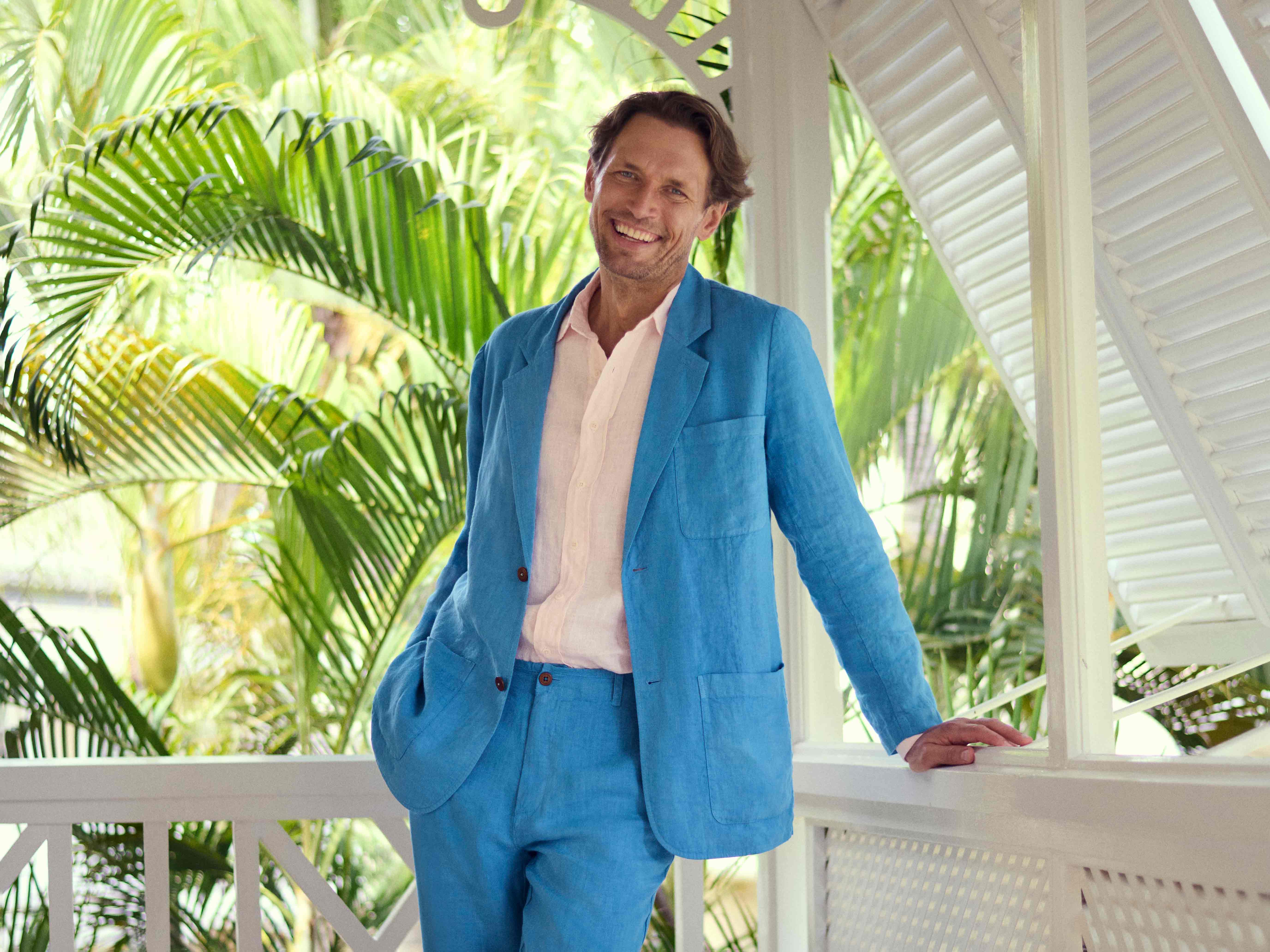 Man in a blue suit standing on a balcony with tropical plants in the background